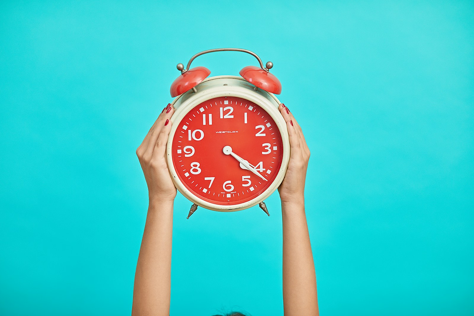 Hire staff person holding red and beige twin bell analog alarm clock