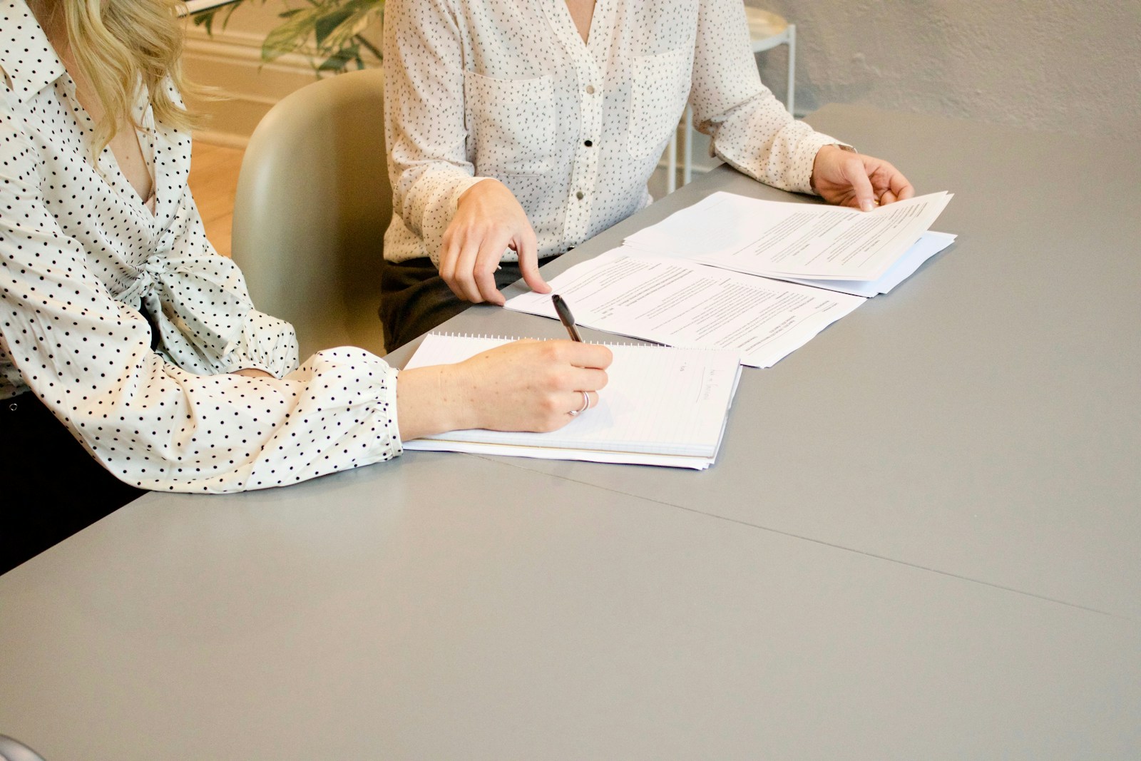 Hire staff woman signing on white printer paper beside woman about to touch the documents