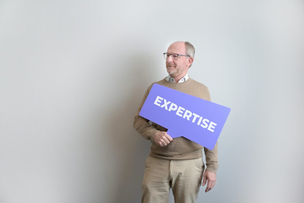 photo by md ishak rahman Man holding an "expertise" sign looking left.